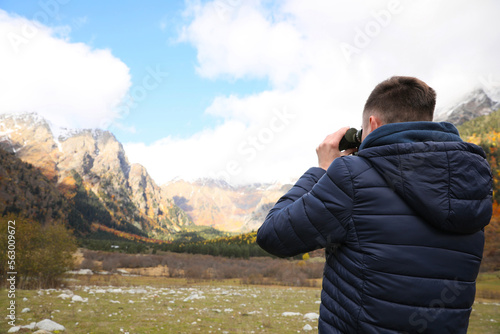 Boy looking through binoculars in beautiful mountains, back view. Space for text
