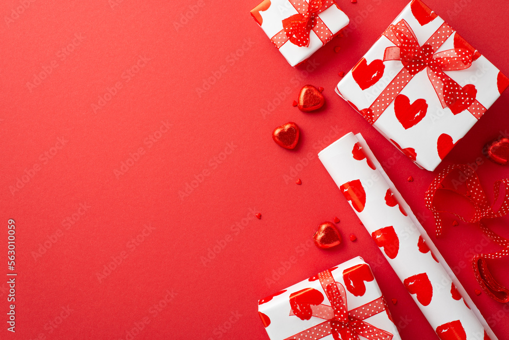Valentine's Day concept. Top view photo of present boxes wrapping paper roll ribbon heart shaped candies and sprinkles on isolated red background with blank space - obrazy, fototapety, plakaty 