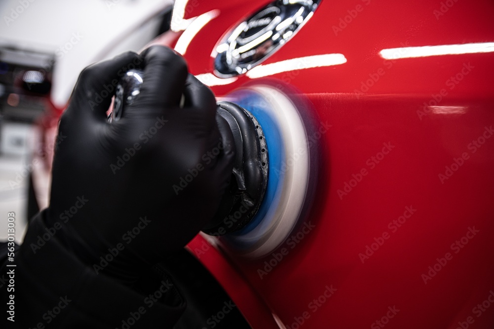employee of a car detailing studio polishes the paintwork of a red car with an electric polishing machine