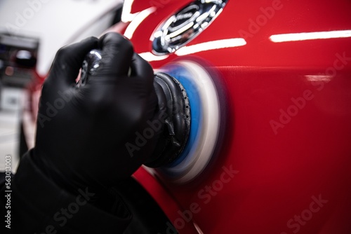 Obraz na płótnie employee of a car detailing studio polishes the paintwork of a red car with an electric polishing machine w salonie