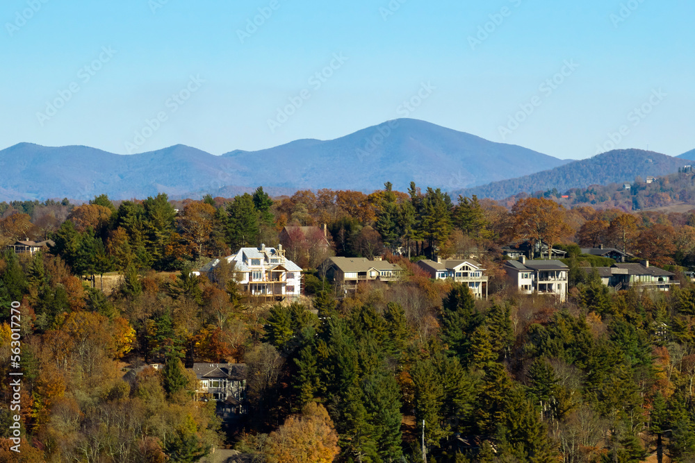 Aerial view of big family houses on mountain top between yellow trees in North Carolina suburban area in fall season. Real estate development in american suburbs