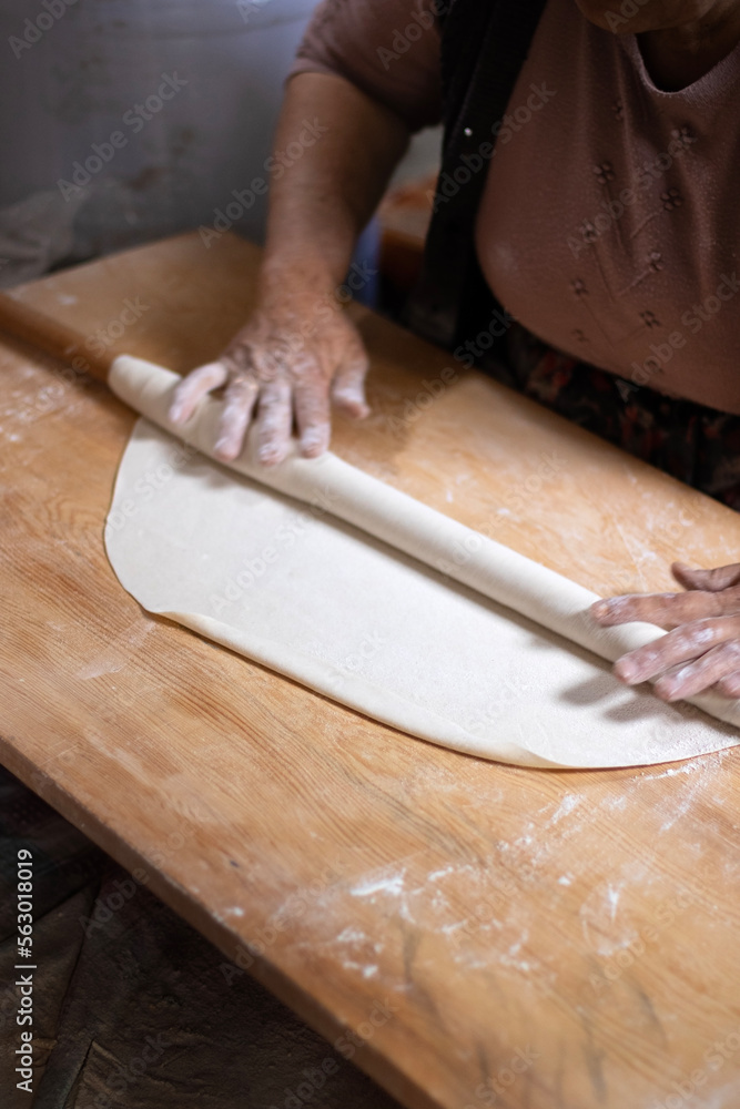 Rolling dough using rolling pin. Women's hands in flour roll out the dough with a rolling pin on the table. Rolling dough using rolling pin. Women's hands in flour roll out the dough with a rolling pin on the table.