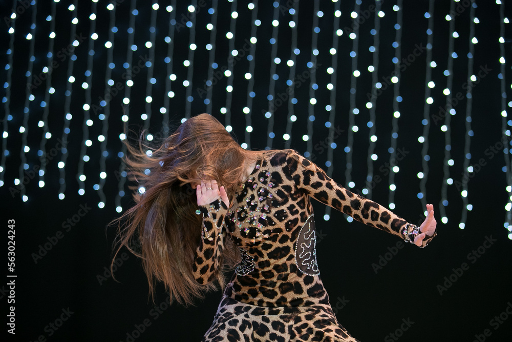 A young dancer with long hair in an oriental costume with a multi-colored shawl poses and dances a belly dance on a concert stage. Professional stage lighting. A young dancer with long hair in an oriental costume with a multi-colored shawl poses and dances a belly dance on a concert stage. Professional stage lighting.