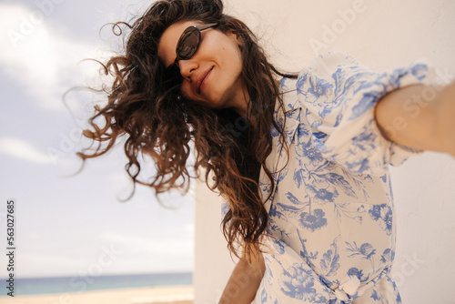Funny young caucasian woman looks at camera  waves her hair outdoor. Brown hair girl wears white shirt and sunglasses. Concept wonderful day  positive moments.