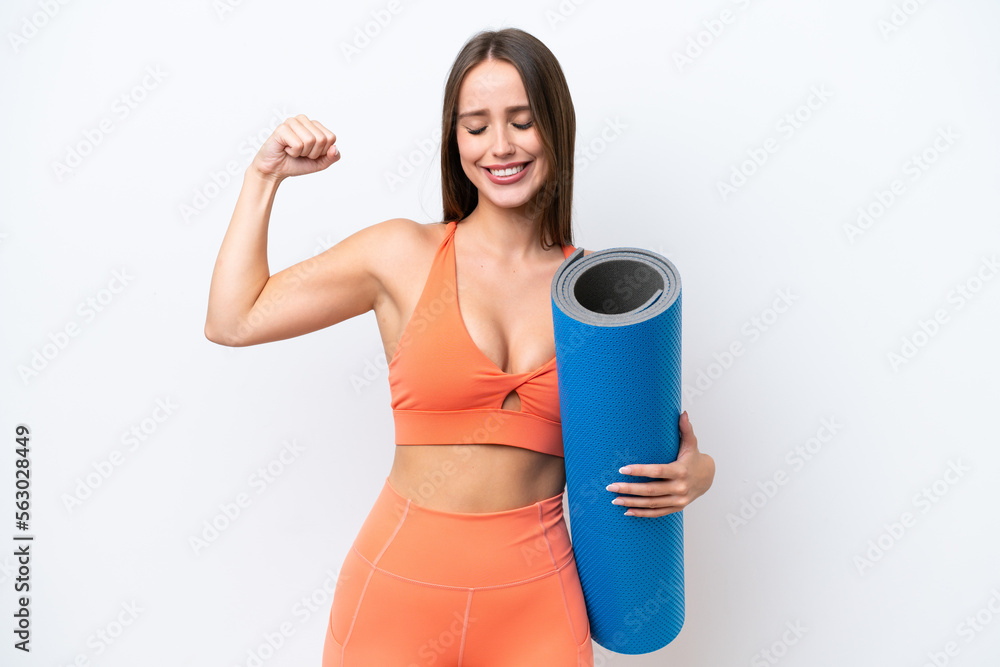 Young beautiful sport woman going to yoga classes while holding a mat isolated on white background doing strong gesture Young beautiful sport woman going to yoga classes while holding a mat isolated on white background doing strong gesture