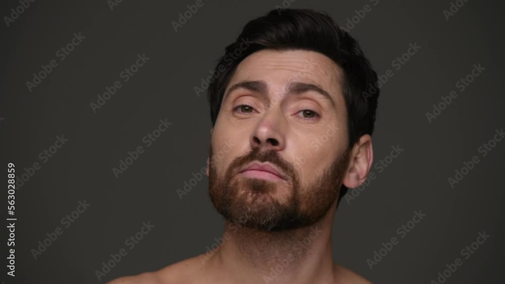 Bearded and shirtless man applying face serum and looking at camera isolated on dark grey Bearded and shirtless man applying face serum and looking at camera isolated on dark grey
