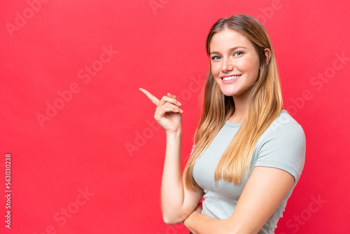 Young beautiful woman isolated on red background pointing finger to the side