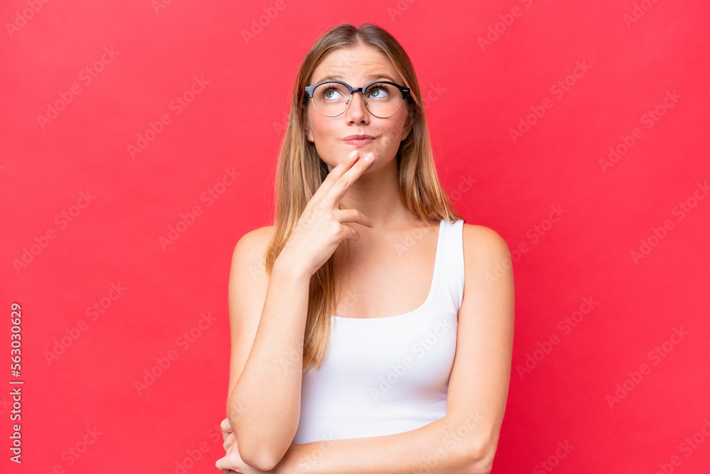 Young beautiful woman isolated on red background looking up while smiling Young beautiful woman isolated on red background looking up while smiling