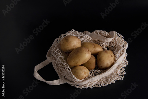 Ripe potatoes in reusable eco-friendly packaging grid on a dark background, little light, dark key. photo