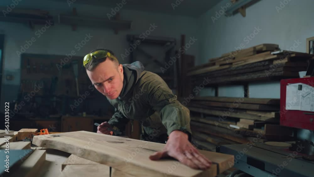 A carpenter in a joinery measures a board to create a wooden product. Woodworker A carpenter in a joinery measures a board to create a wooden product. Woodworker