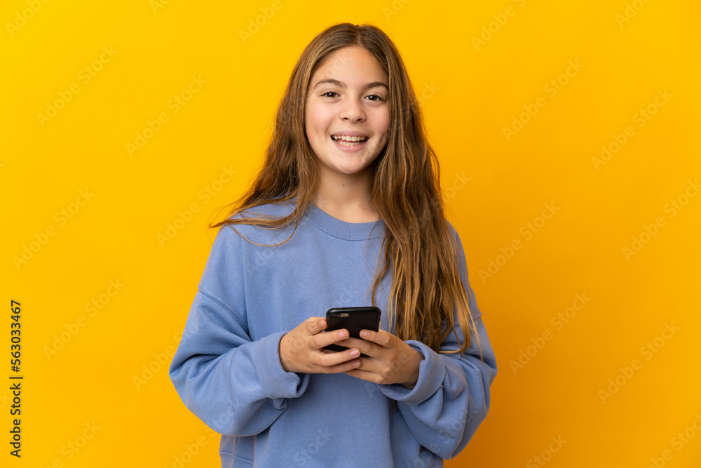 Child over isolated yellow background surprised and sending a message Child over isolated yellow background surprised and sending a message