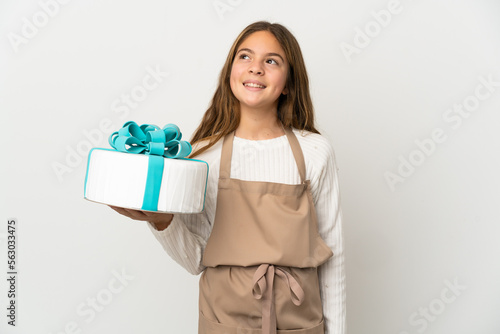 Little girl holding a big cake over isolated white background thinking an idea while looking up