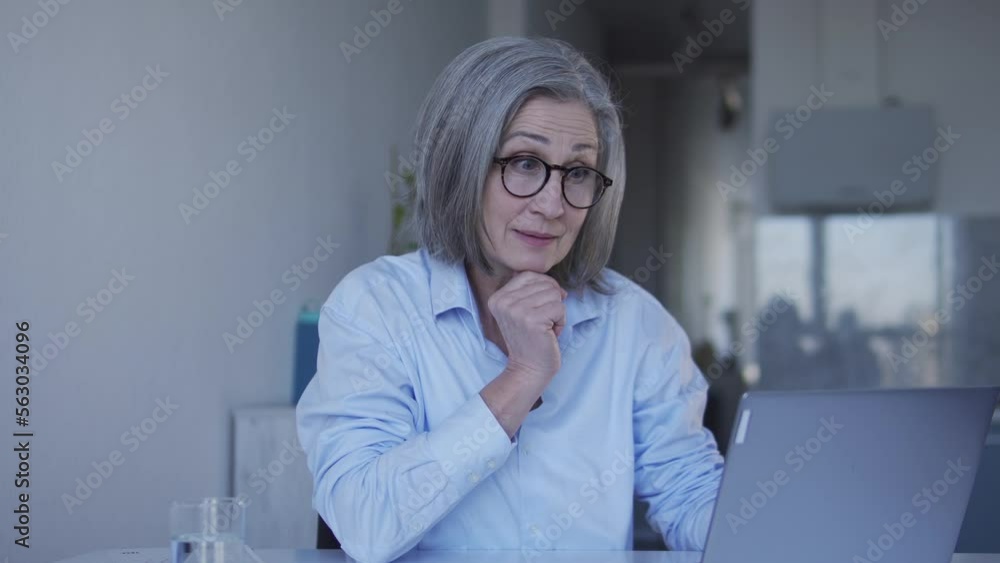 Successful attractive woman in her 60th working on laptop sitting at home office, project manager working on manage of the project as a whole, controlling all processes and communications Successful attractive woman in her 60th working on laptop sitting at home office, project manager working on manage of the project as a whole, controlling all processes and communications