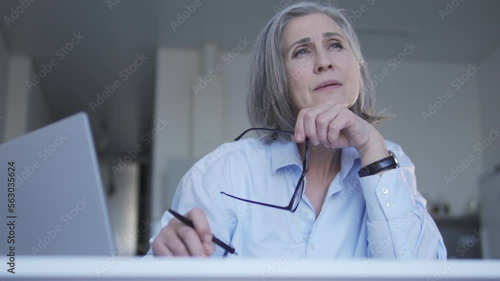 Lady boss with gray hair looking through annual report her employees sent, dissatisfied with results, taking off eyeglasses to calm painful eyes and contemplating about business improving Lady boss with gray hair looking through annual report her employees sent, dissatisfied with results, taking off eyeglasses to calm painful eyes and contemplating about business improving