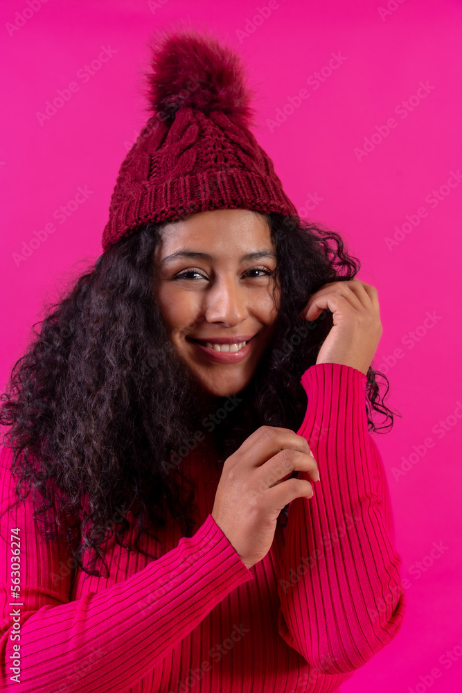Curly-haired woman in a wool cap on a pink background portrait smiling, studio shot Curly-haired woman in a wool cap on a pink background portrait smiling, studio shot
