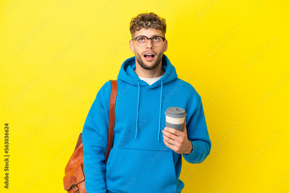 Young student blonde man isolated on yellow background looking up and with surprised expression Young student blonde man isolated on yellow background looking up and with surprised expression