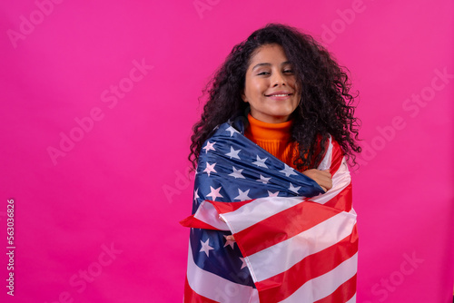 Portrait of a curly-haired woman smiling with the usa flag on a pink background, studio shot