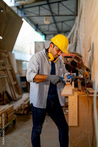 Caucasian wood working or carpenter man use electrical saw to work with timber in factory workplace and wear safety clothes to protect himself. photo