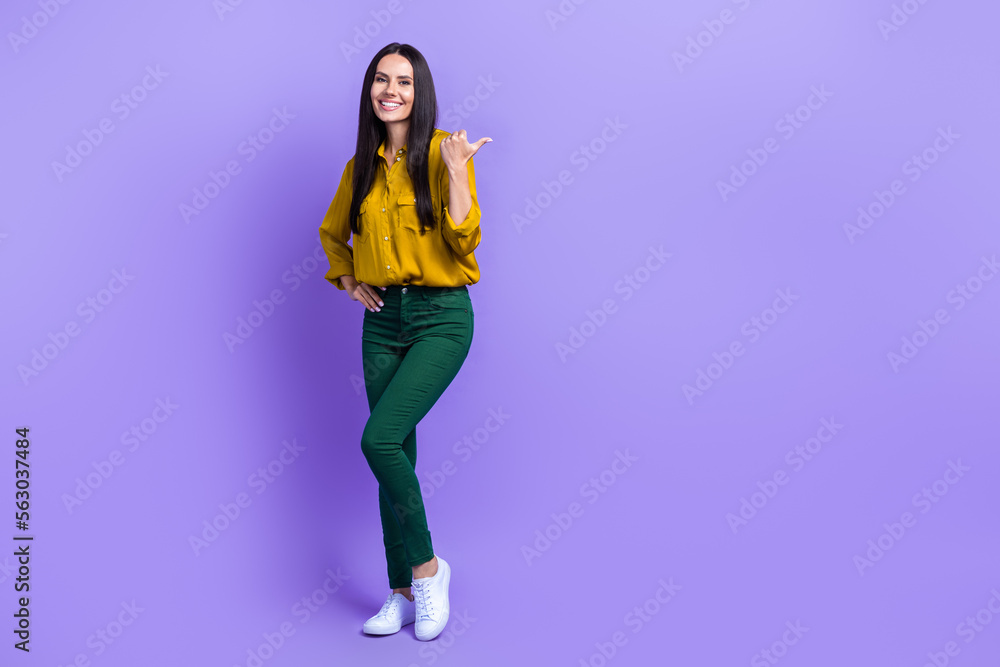 Full length portrait of charming cheerful person direct thumb finger empty space isolated on purple color background Full length portrait of charming cheerful person direct thumb finger empty space isolated on purple color background