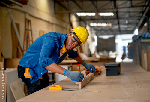 African American carpenter man use pencil to mark on timber during work with in wood factory workplace.