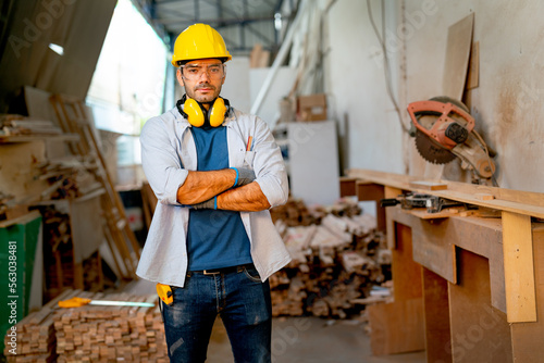 Caucasian carpenter man stand with arm-crossed or confidence action and look at camera in front of stack of timber and carpenter equipment in factory workplace. photo