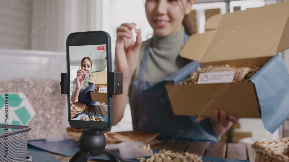 SME owner go green net zero retail store live stream talk on phone showing eco care plastic free packaging box. Asia people young woman record video on tiktok IG reel instagram shop happy side hustle.