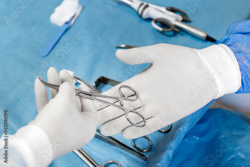 A nurse's hand passes a surgical instrument to a surgeon's hand during a patient operation
