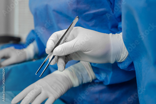 Medical tweezers in surgeon's hand in white gloves during an operation on a patient