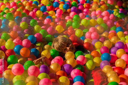Little smiling boy playing lying in colorful balls park playground