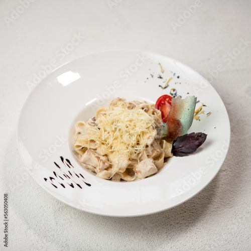 Portion of pasta pappardelle with cheese and cream sauce in plate on white background. Decorated with basil and tomato Italian food. View from above. Serving dish. 