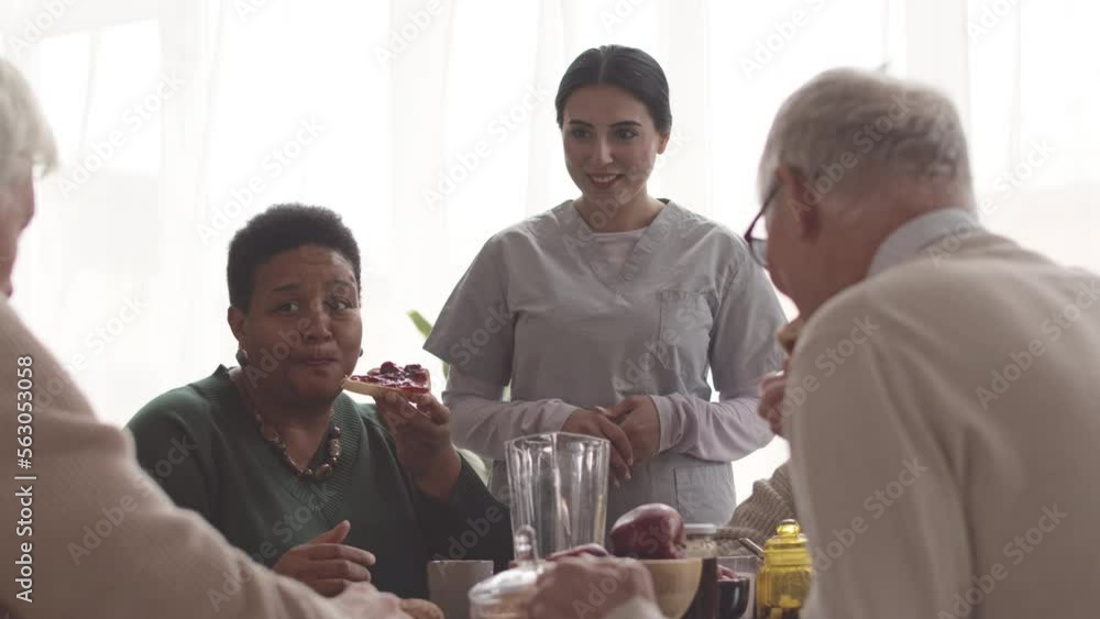 Multiethnic boomers having breakfast together at nursing home with young female nurse taking care of them Multiethnic boomers having breakfast together at nursing home with young female nurse taking care of them