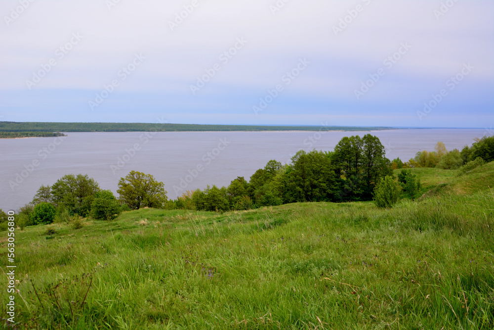green rolling hill with green trees and Volga river and rainy sky on background