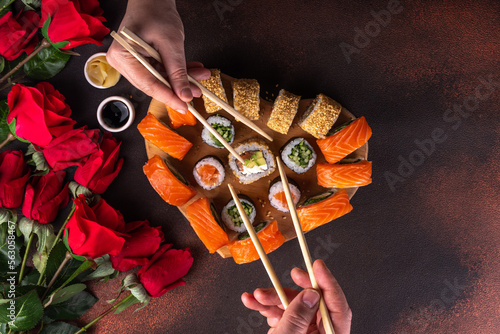 Heart shaped Valentine day sushi set. Classic sushi rolls, philadelphia, maki set for two, with two pairs of chopsticks for Valentine\'s dating dinner, with rose flowers bouquet on dark background