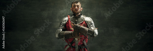 Banner. Serious brutal bearded man, medieval warrior and knight with dirty wounded face holding big sword over dark background. Concept of courage, history