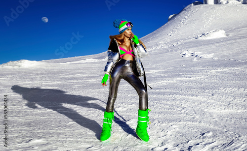 Sexy girl in silver cosmic outfit silver and winter boots is posing in the mountains. Female model in glamour silver jumpsuit in winter scenery. photo