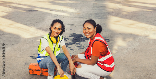 Two african american female workers  match smiling buddy riends working at container station sitting on toolbox informal together on the road in container yard traveling repairing container friendship photo