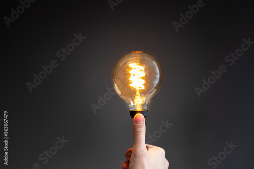 Symbol for saving energy. Hand holds a filament light-bulb where the light intensity is low.
