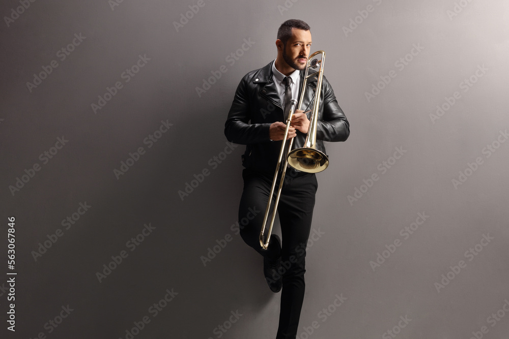 Fototapeta premium Young man with a trombone standing and leaning on a wall