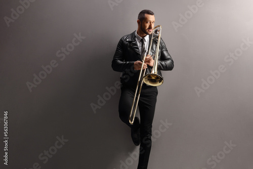 Young man with a trombone standing and leaning on a wall