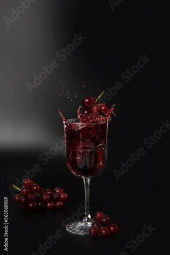 Red wine is poured into a wine glass on a black background with grapes and splash