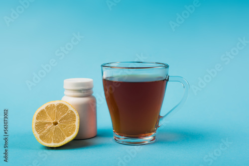 Cup of tea near lemon and pills on blue background.
