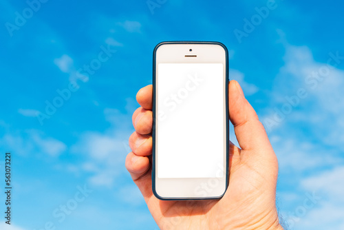 Mockup image of hand holding white mobile phone with blank white screen in blue sky white cloud background.Copy space.