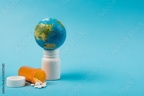Small globe on globe with pills from new omicron strain on blue background.