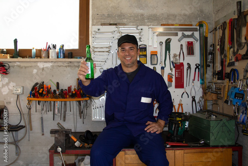 Image of a smiling craftsman in his workshop holding a bottle of beer. Time to relax and refresh after work.
