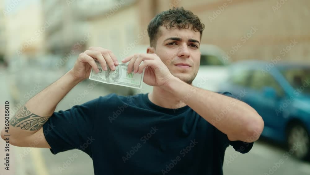 Young hispanic man breaking 100 dollars banknote at street Young hispanic man breaking 100 dollars banknote at street