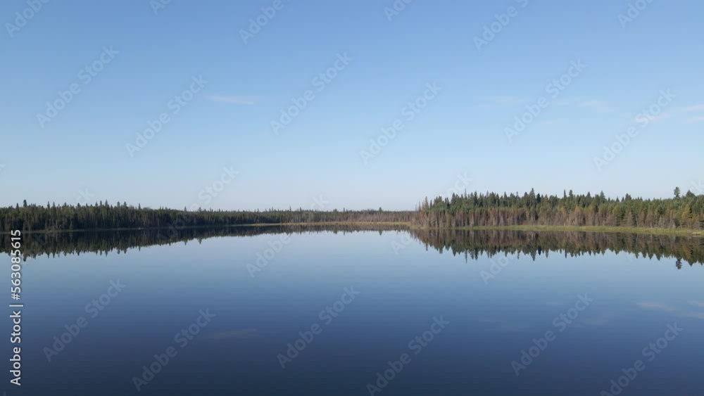 Drone moving very slowly forward above a calm lake that is reflecting the blue sky with a few small clouds. The shore of the lake is lined with evergreen trees.
Drone moving very slowly forward above a calm lake that is reflecting the blue sky with a few small clouds. The shore of the lake is lined with evergreen trees.