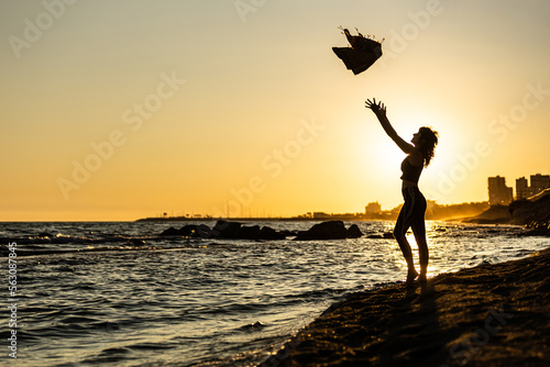 woman throwing the towel on the beach at sunset with the golden sun and the city in the background