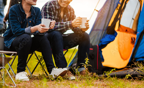 Fotografia Happy Asian young couple sitting on picnic chair drinking tea and coffee while tent camp lakeside at parks outdoors on vacation holiday