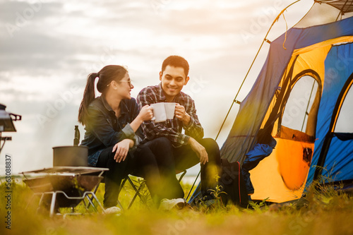 Happy Asian young couple sitting on picnic chair drinking tea and coffee while tent camp lakeside at parks outdoors on vacation holiday. Adventure lifestyle of man and woman with camping in nature. © Day Of Victory Stu.