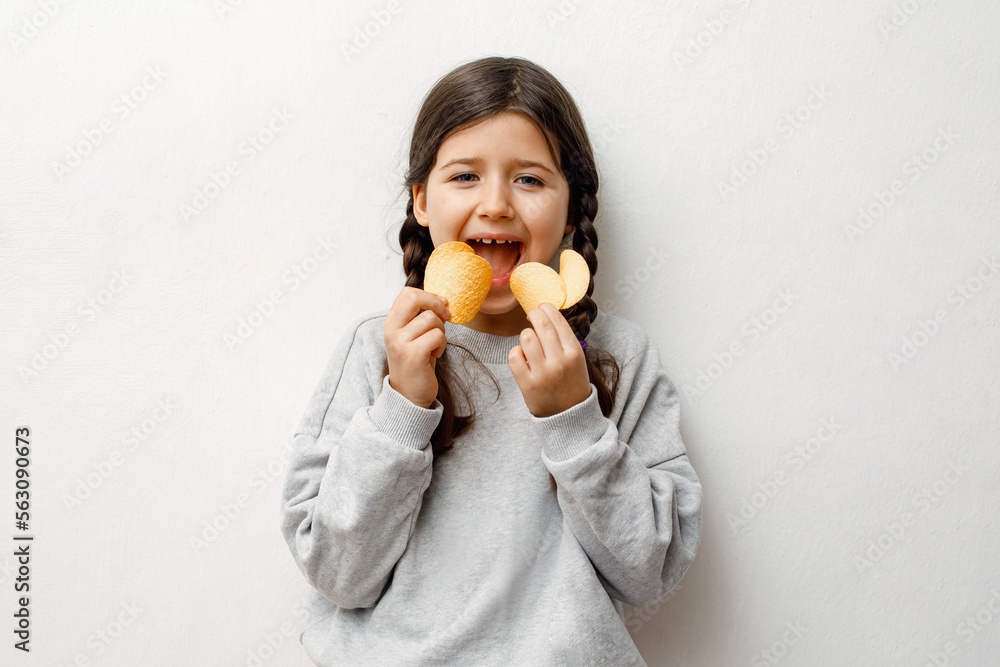 a little caucasian girl eats chips with an appetite, opening her mouth wide, fast food, junk food a little caucasian girl eats chips with an appetite, opening her mouth wide, fast food, junk food